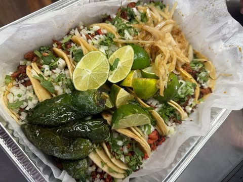A tray of handmade tacos topped with roasted jalapeño, lime, diced onion and fresh cilantro